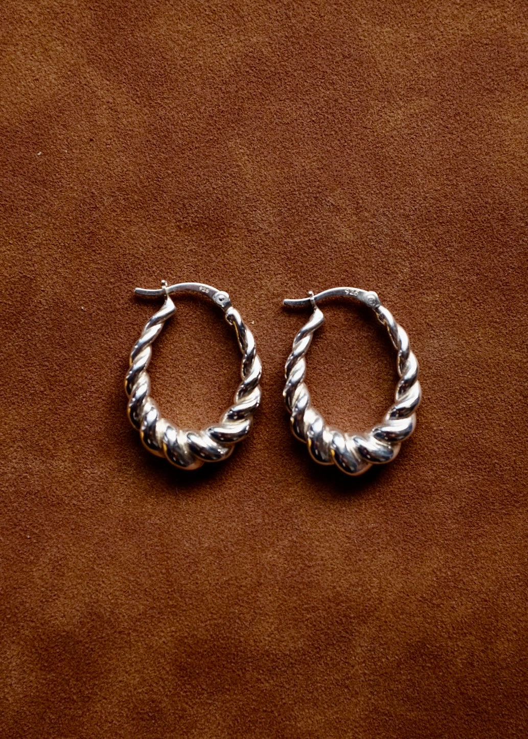 Pair of silver hoop earrings on a brown leather background