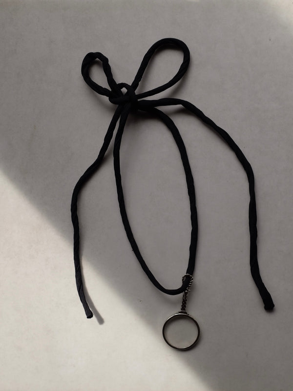 Black cord necklace with a round pendant on a light gray background