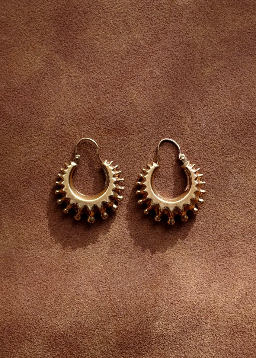 Pair of gold hoop earrings on a brown leather surface
