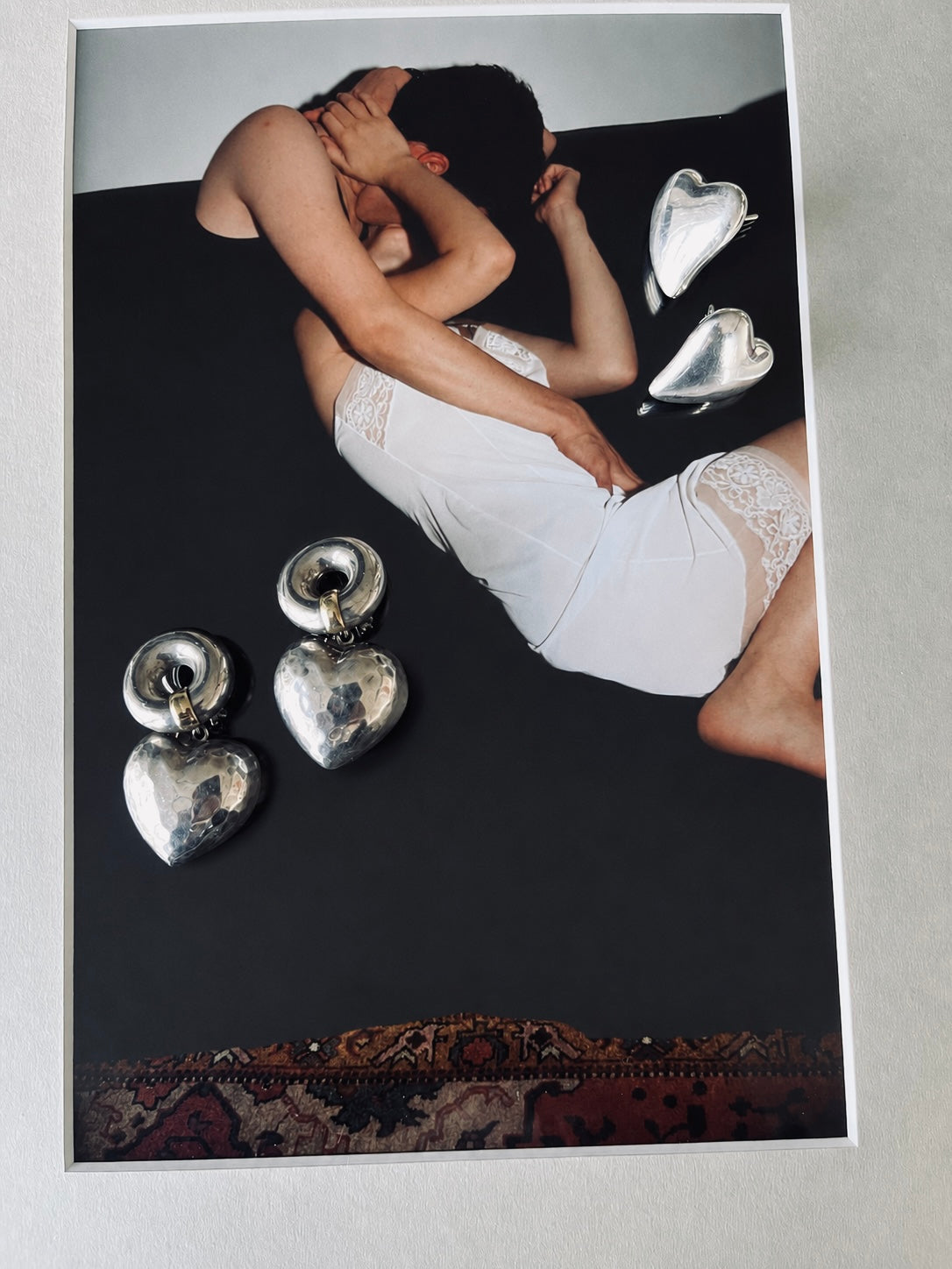 Person in white underwear lying on a dark surface with silver heart-shaped objects.
