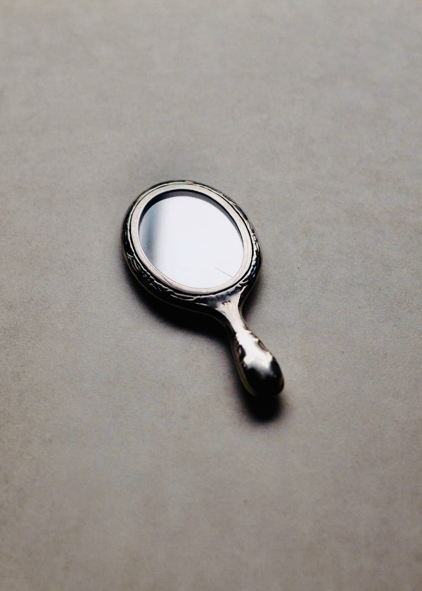 Small round mirror with a handle on a gray surface