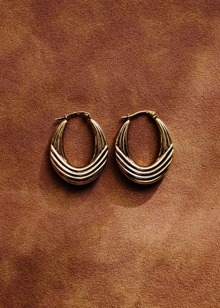 Pair of gold hoop earrings on a brown leather surface