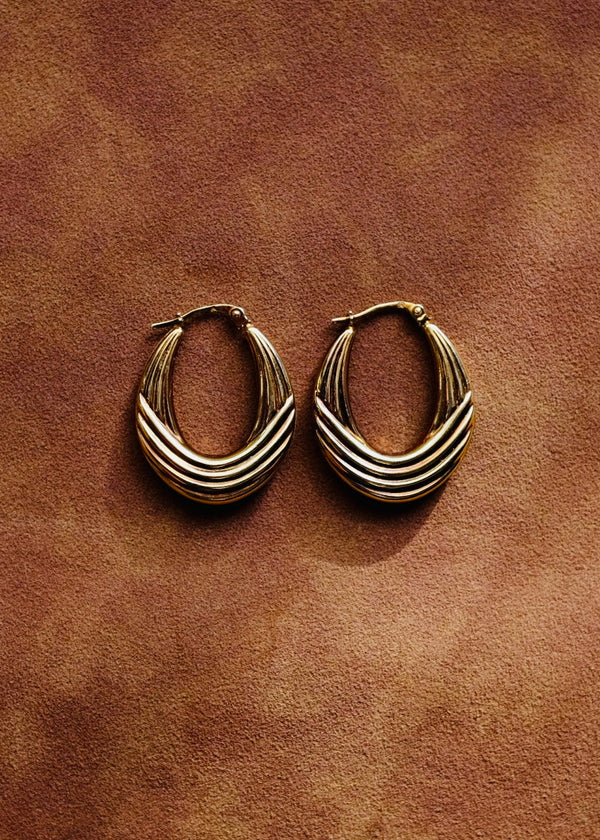 Pair of gold hoop earrings on a brown leather surface