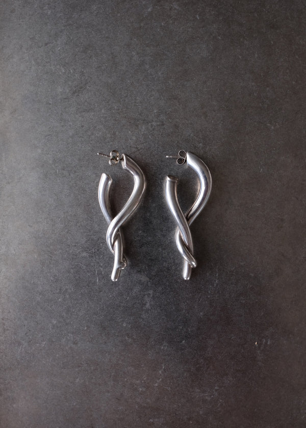 A pair of silver-toned twisted hoop earrings with post backings, displayed on a dark textured slate surface.