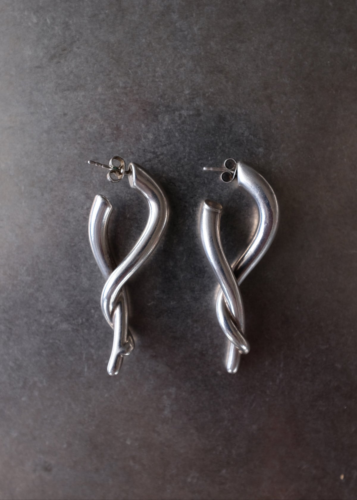A pair of polished silver twisted hoop earrings with post backings, displayed on a dark textured surface.