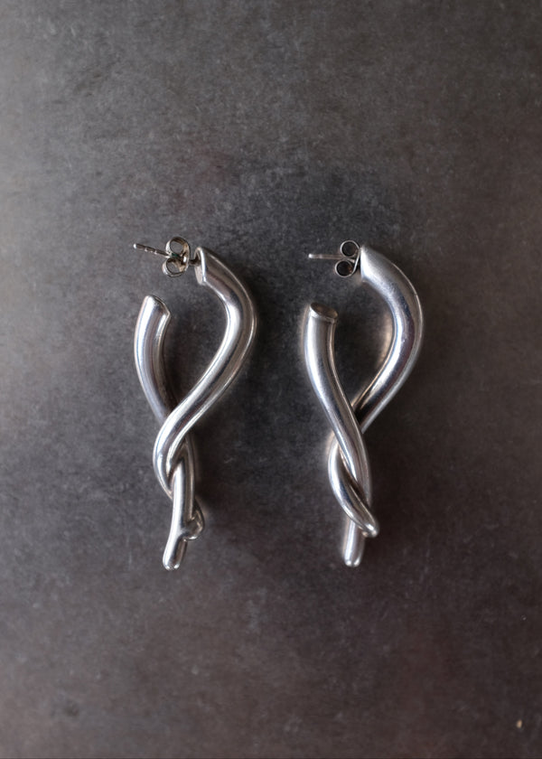 A pair of polished silver twisted hoop earrings with post backings, displayed on a dark textured surface.