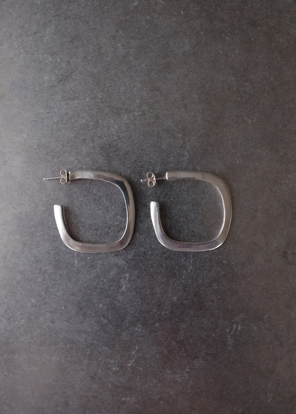 A pair of silver-toned square hoop earrings with post backs, displayed on a dark textured gray surface.
