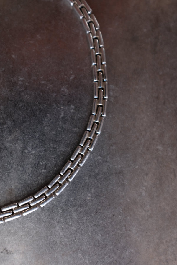 A close-up of a silver-toned metal link chain, likely a bracelet or necklace, arranged in a curve on a dark textured gray surface.