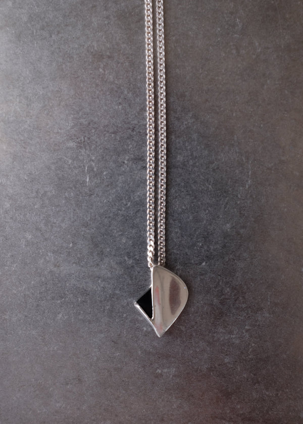 A close-up of a silver chain necklace with a polished teardrop-shaped pendant resting on a dark gray textured surface.