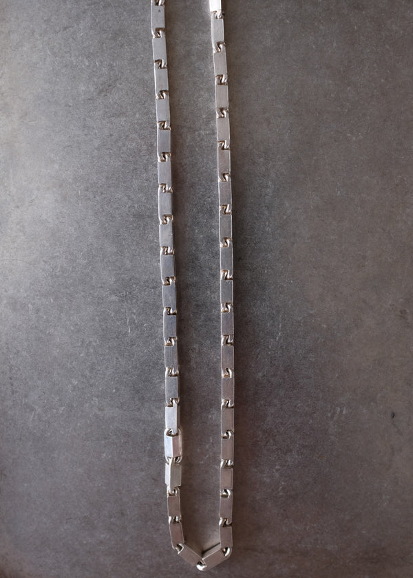 A silver-toned metal link chain necklace laid flat on a textured gray surface.