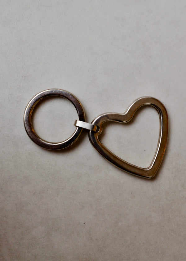 Metal keychain with heart and circular design on a beige background