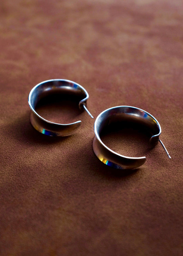 Pair of silver hoop earrings on a brown leather surface