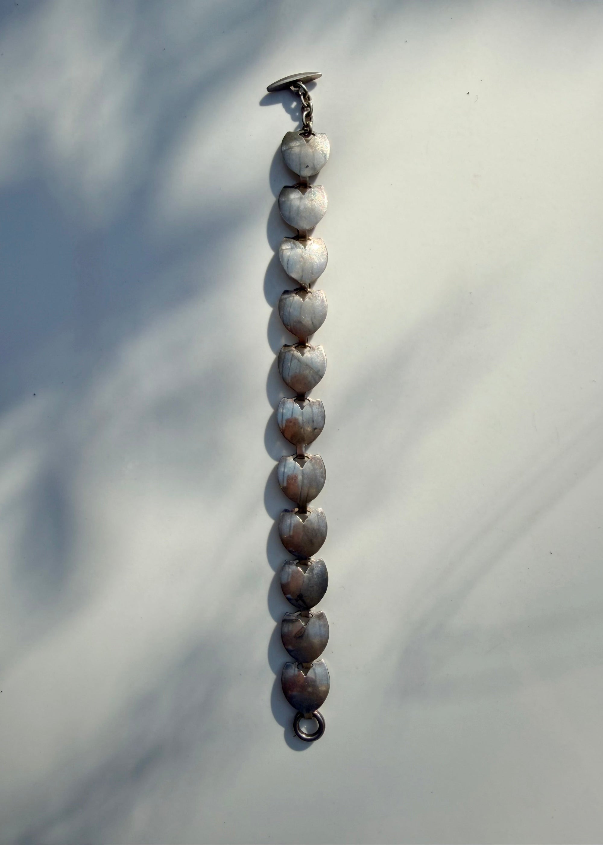 A long beaded necklace made of polished shell beads, laid vertically on a light gray surface with soft shadows.