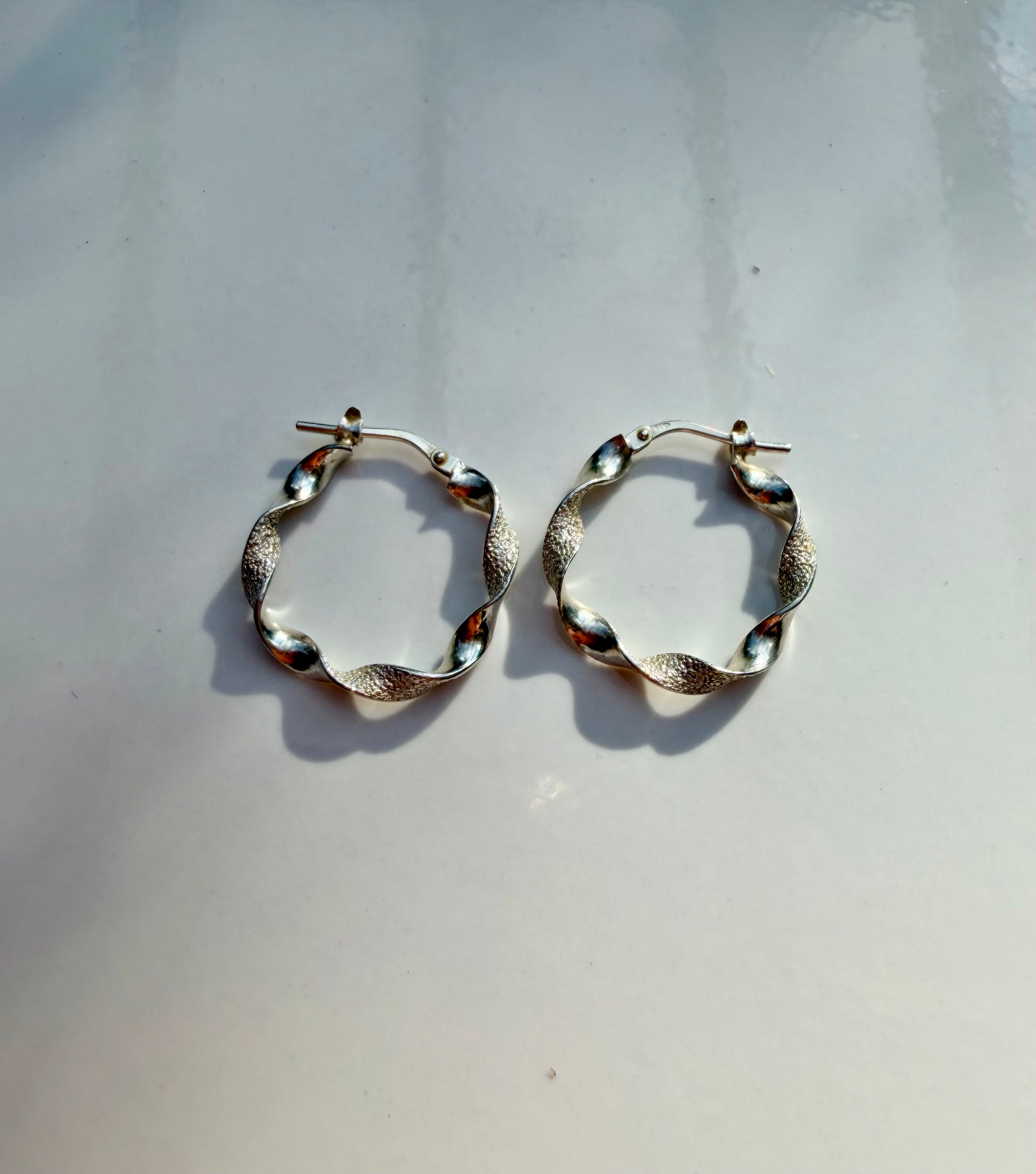 A pair of textured silver hoop earrings with small reflective bead accents, displayed on a light gray surface.