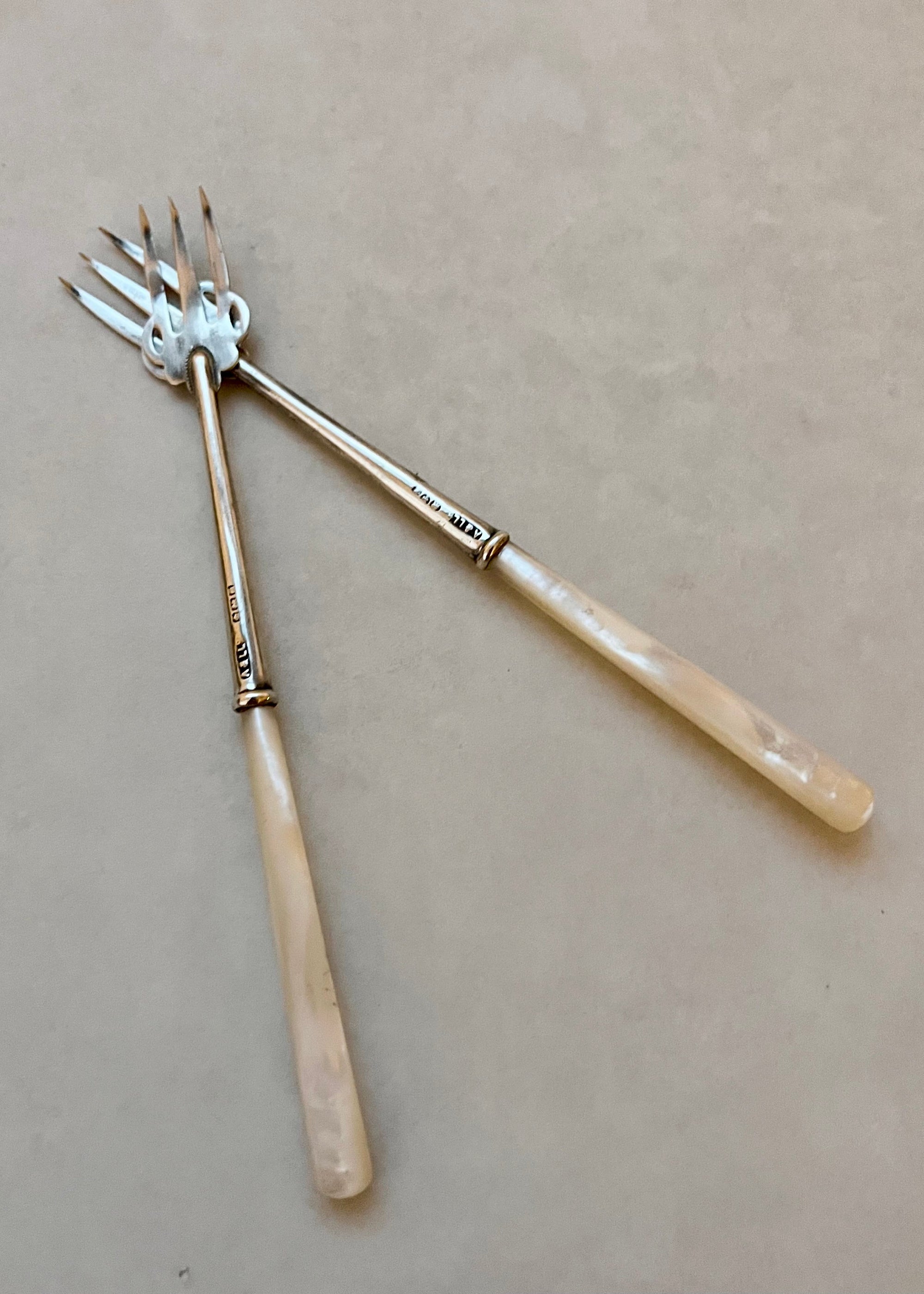 Two silver forks with decorative handles on a beige background