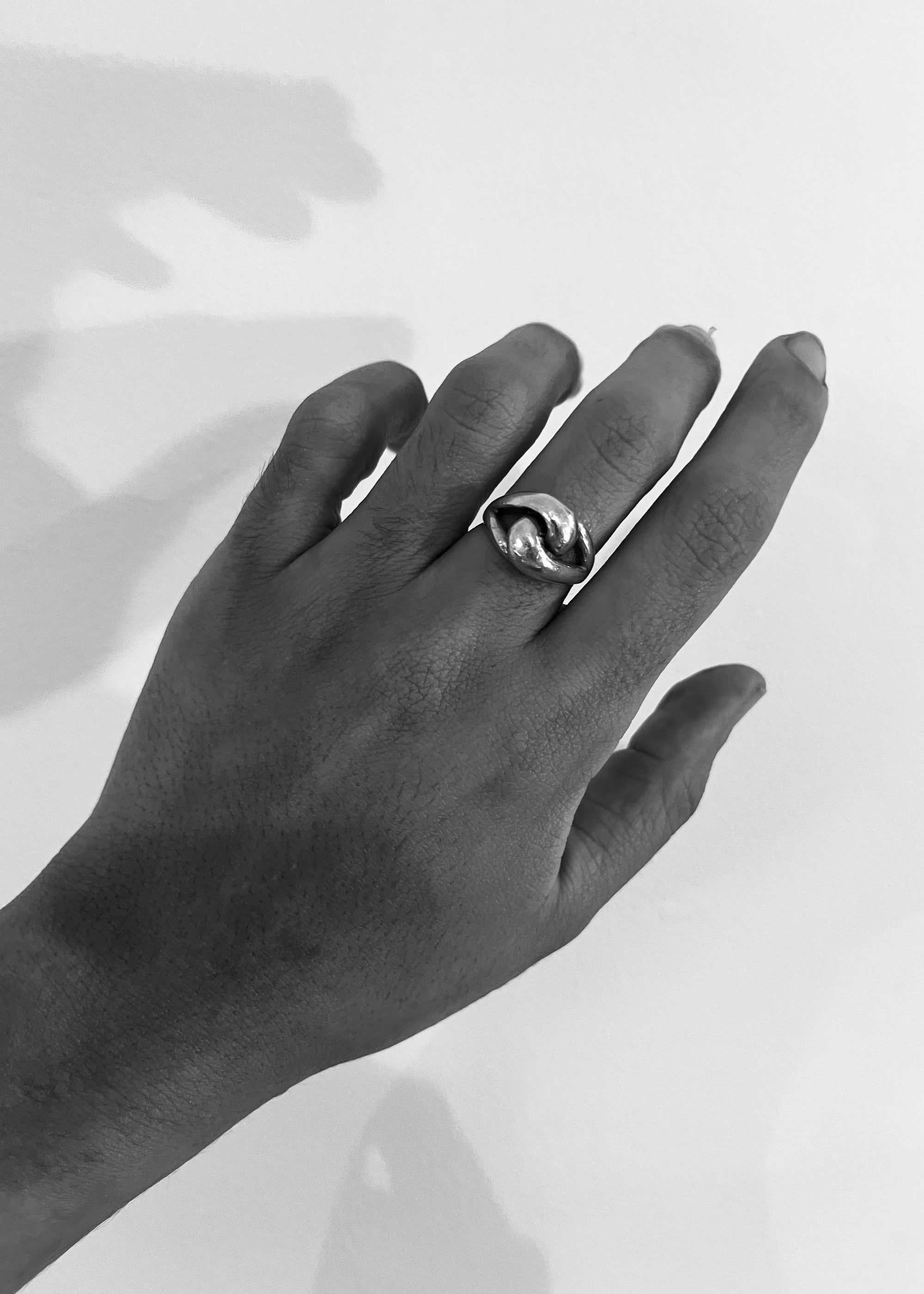 Hand wearing a silver ring with a clear gemstone on a light background