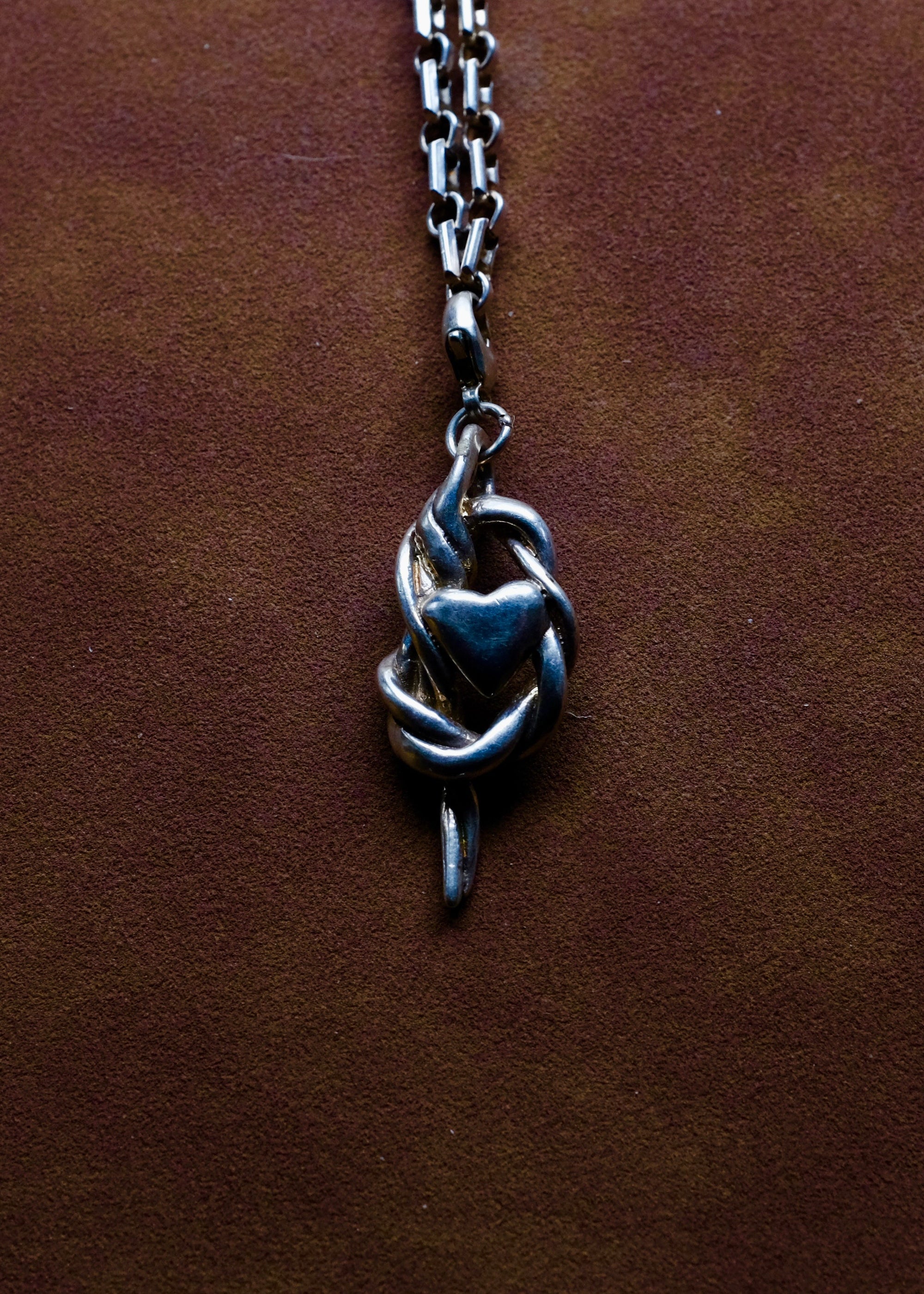 Silver necklace with a heart and knot pendant on a brown leather surface