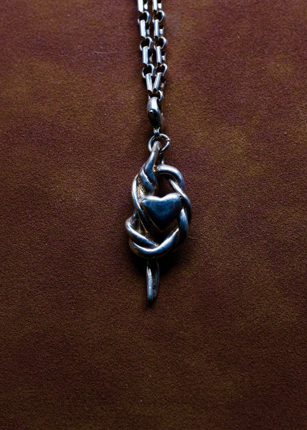Silver necklace with a heart and knot pendant on a brown leather surface
