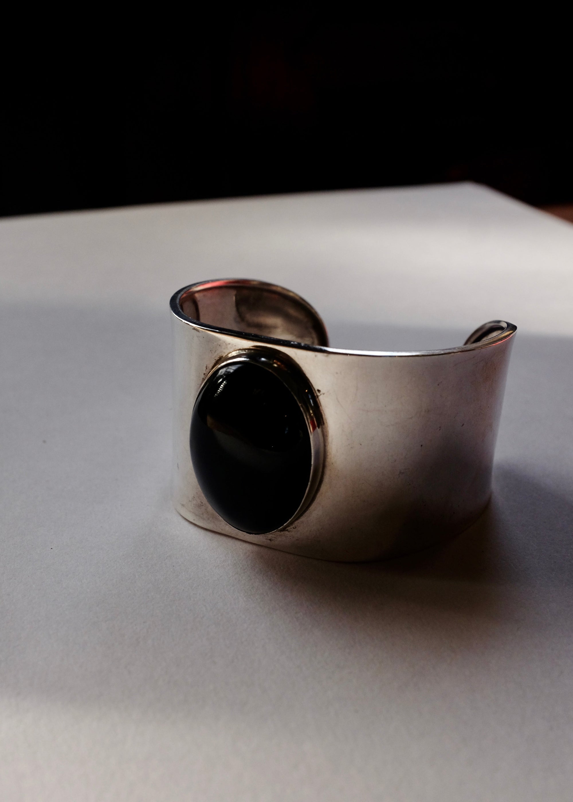 Silver cuff bracelet with a black stone on a light gray surface