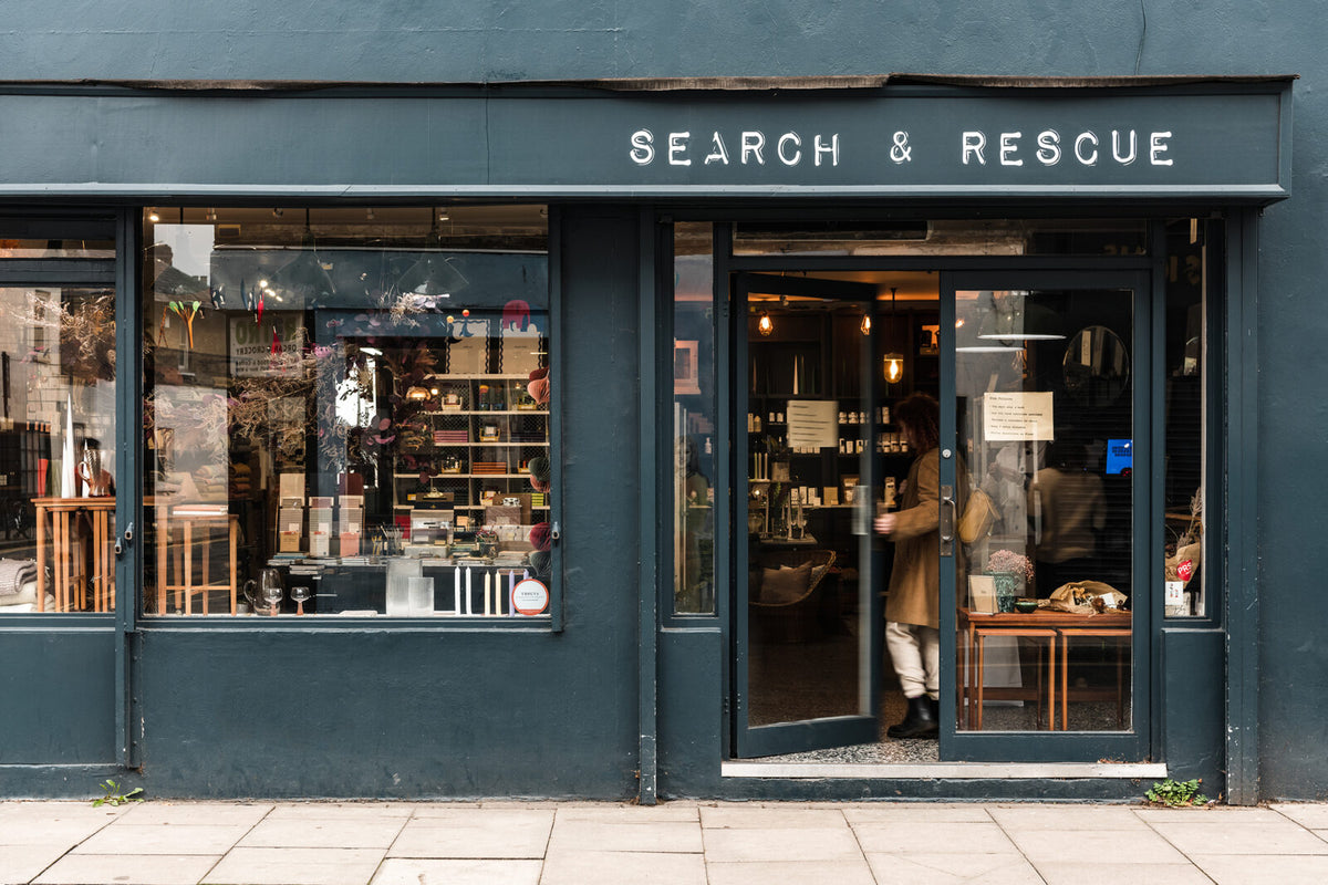 A storefront with a dark teal facade and large windows. White text above the entrance reads 'SEARCH & RESCUE'.